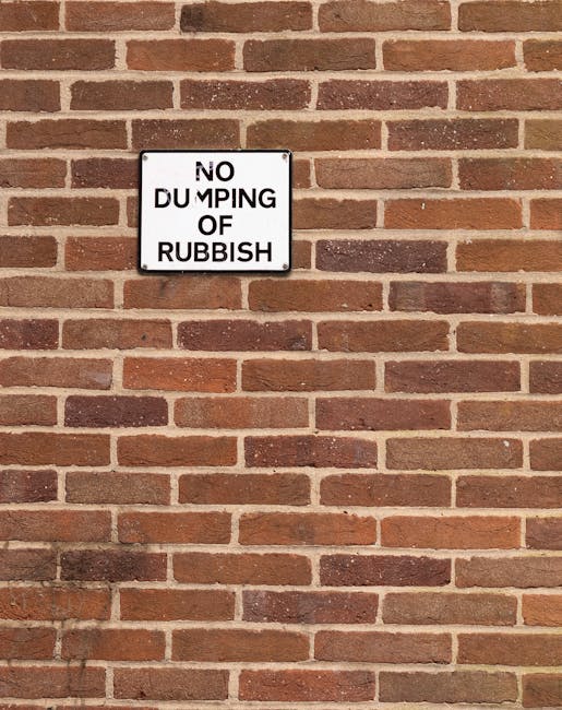 A large pile of mixed waste materials, including black and black-and-white rubbish bags, flattened cardboard boxes, and loose paper and packaging items, situated on a paved roadside area in front of a
